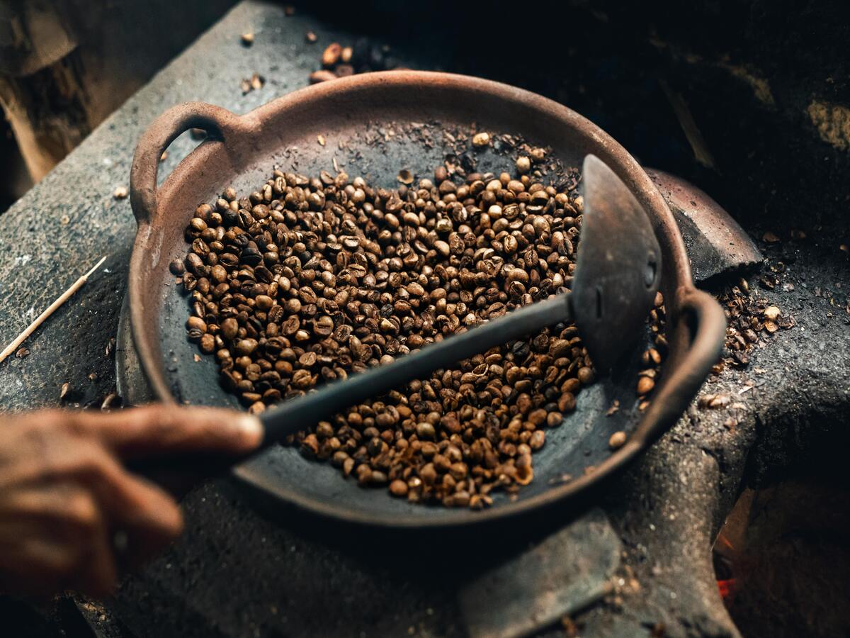 An image of coffee beans roasting in a rusty Chinese wok.