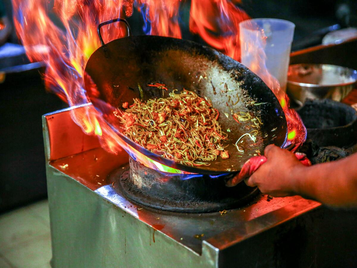 A person cooking noodles in a Chinese wok.