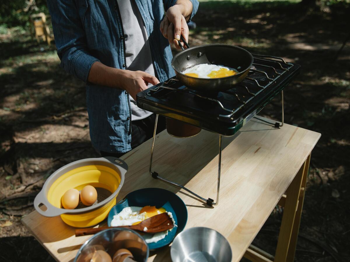 A man frying eggs outdoors on older cookware.