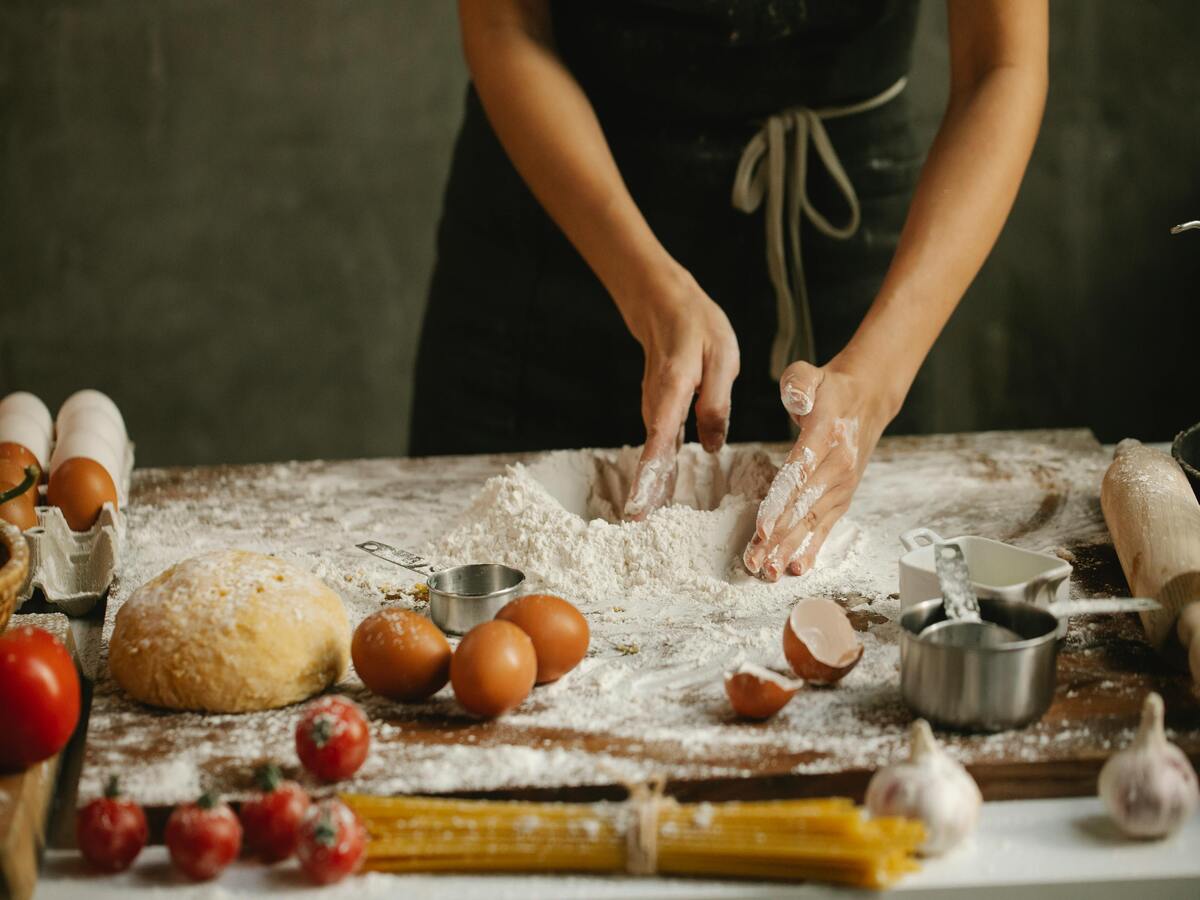 A woman making dough on a table with a rolling pin in front of a cutting board.