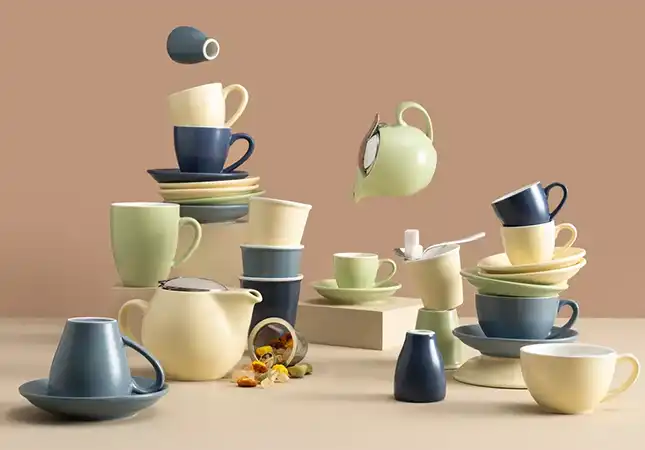 Bevande collection of café ceramics in Aegean, Sapphire, Avorio, and Menta — cups, saucers, teapots, and jugs stacked in a modern display